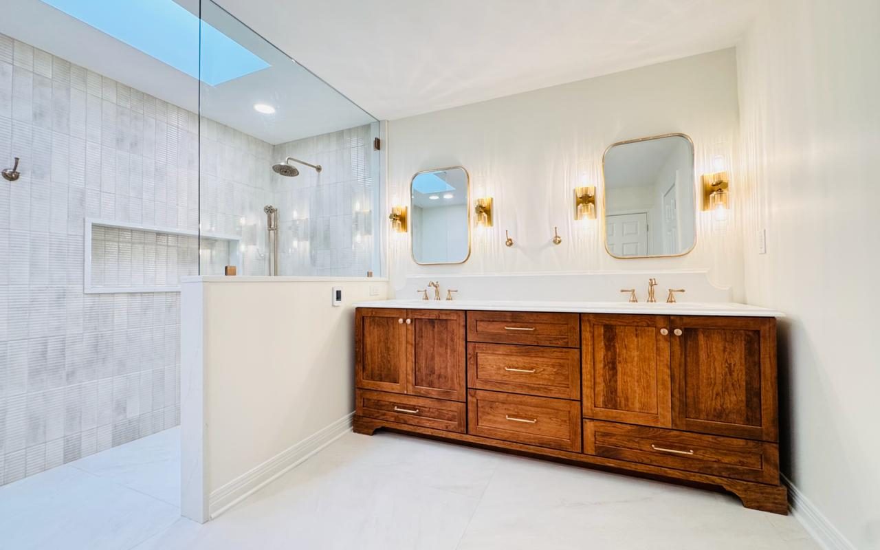 Finished primary bath after the Wilson Way remodel — walnut double vanity, frameless glass shower, brass fixtures