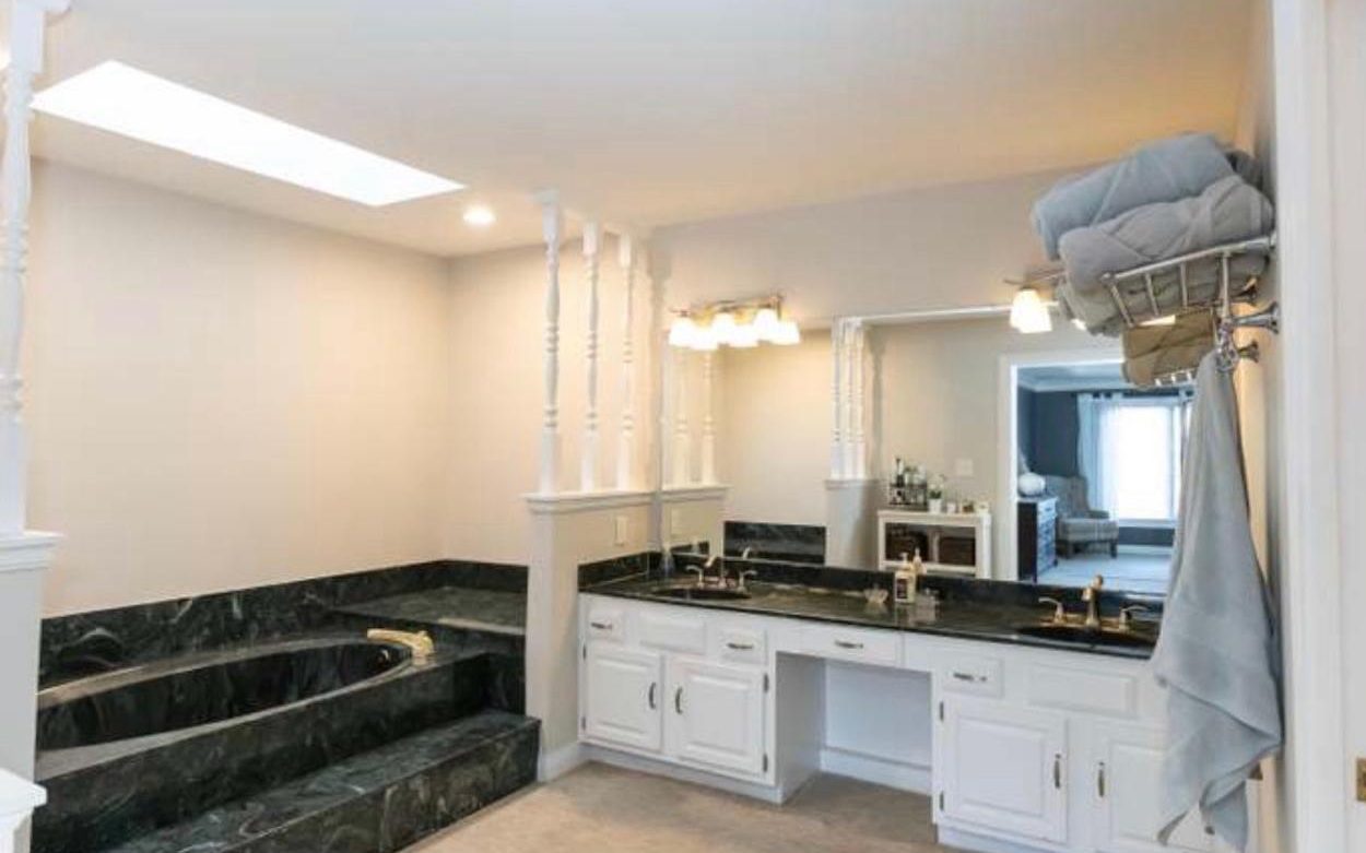 Primary bath before the Wilson Way remodel — green-marble sunken tub, white vanity, dated lighting